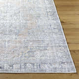 Close up of a gray and prairie dust Yachi Washable Area Rug on a wood floor, showing the traditional pattern and woven texture. Front