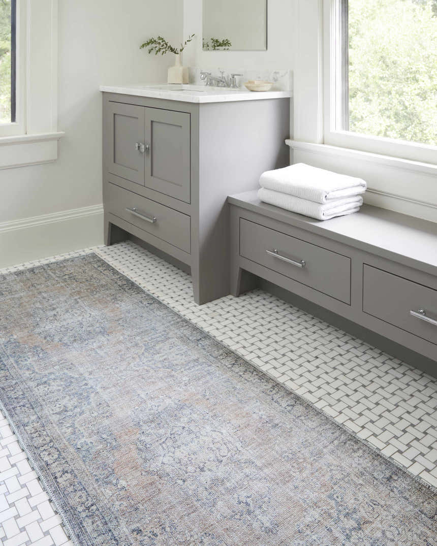 Bathroom scene with gray vanity and Yachi Washable Area Rug in gray, silver and prairie dust colors on white tile floor. Roomscene-Runner