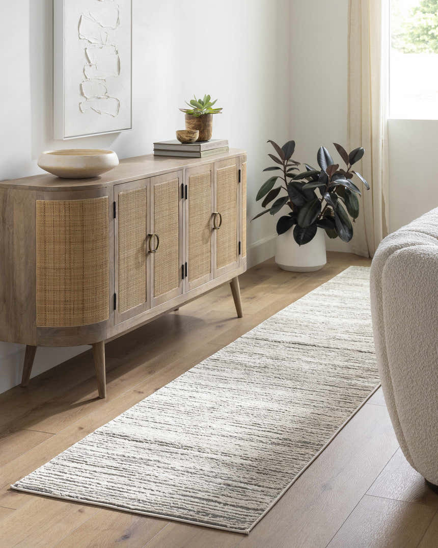 Living room scene with a Yemassee Tibetan Striped Area Rug, wood cabinet, plant, and neutral sofa. Modern, cozy style. Roomscene-Runner