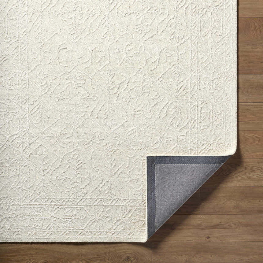 Close-up of the Yadid Cream Wool Area Rug showing its subtle floral pattern and hand-tufted texture on a wood floor. Fold
