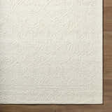 Close-up of the Yadid Cream Wool Area Rug showing its hand-tufted texture and subtle traditional pattern on a wood floor. Corner