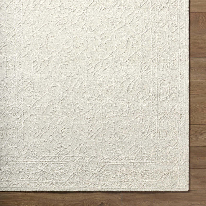Close-up of the Yadid Cream Wool Area Rug showing its hand-tufted texture and subtle traditional pattern on a wood floor. Corner