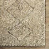 Close up of the hand-tufted Yurem Area Rug. Beige wool rug with a geometric diamond pattern and a soft, shaggy texture. Corner