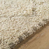 Close-up of the hand-tufted Yurem Area Rug. Beige, cream, and tan wool fibers create a soft, textured pile. Texture