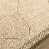 Close-up of the hand-tufted Addien Area Rug. Neutral beige wool rug with subtle geometric line pattern and textured border. Texture