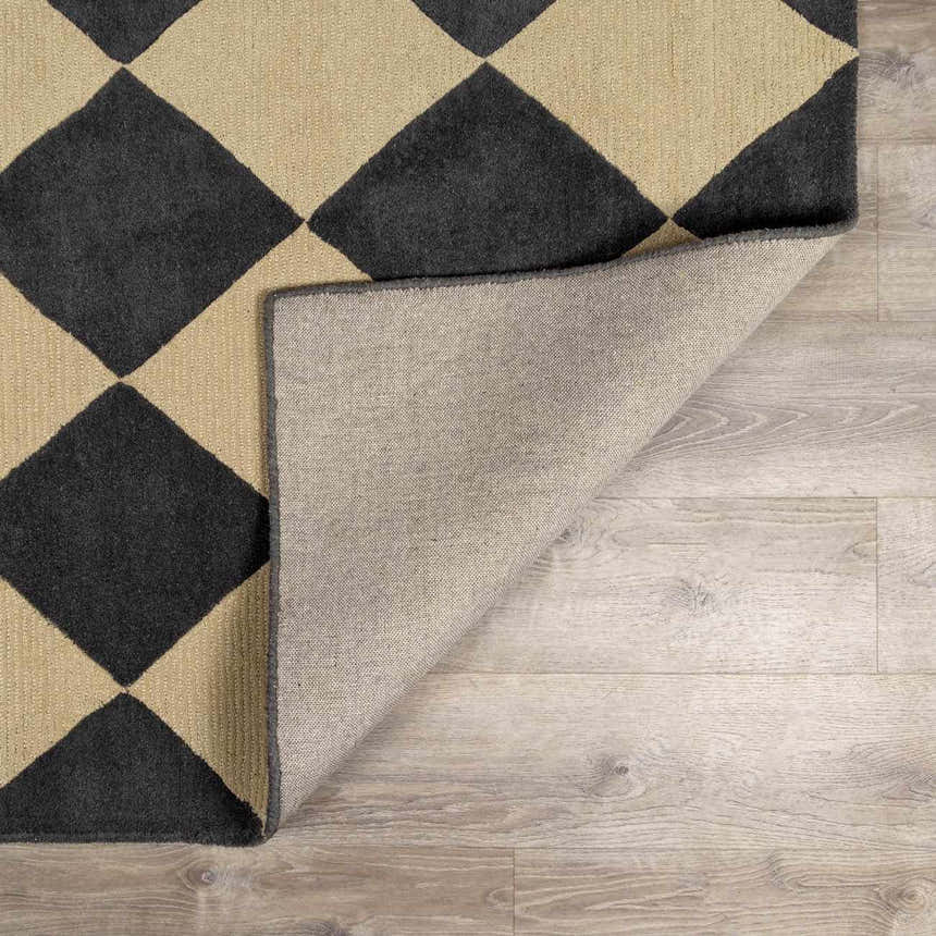 Close-up of Aradia Charcoal Area Rug showing diamond pattern, wool texture, and rug backing on light wood floor. Fold