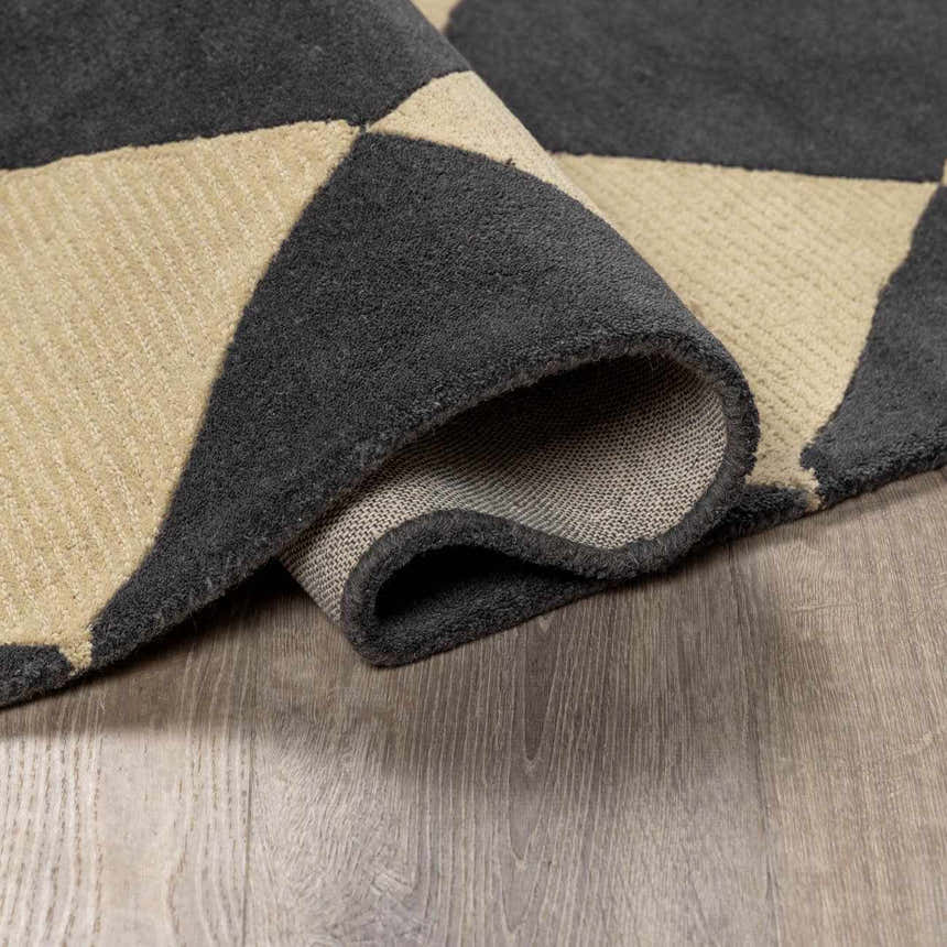 Close-up of the hand-tufted Aradia Charcoal Area Rug showing its wool texture and geometric pattern in charcoal and beige. Fold