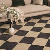 Living room scene with a beige sofa and the Aradia Charcoal Area Rug featuring a bold, modern checkerboard pattern. Styleshot