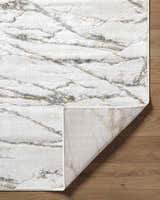 Close-up of the Zelah Area Rug featuring a beige, charcoal, and gold marble-like pattern on a wooden floor. Fold