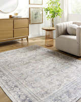 Living room scene with light wood floors, Zahar Washable Area Rug in light silver, gray, and cream, and a beige chair. Roomscene-Rectangle