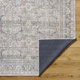 Close-up of Zahar Washable Area Rug showing traditional light silver, gray, and warm gray pattern and texture on wood floor. Fold