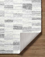 Close-up of the Alaura Area Rug showing its ivory and gray shag texture and machine-woven construction. Fold