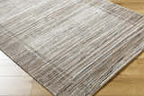 Close-up of Ainhoa Luxe Thick Area Rug. Contemporary style rug in black, ivory, peach, and tan on wood floor. Corner