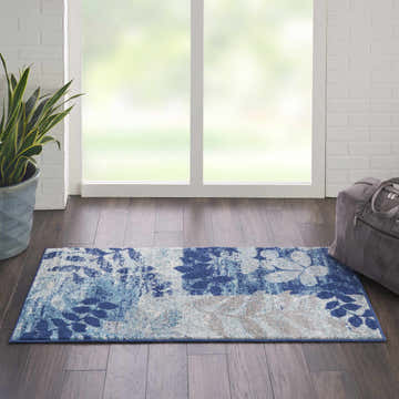 Bright room scene with Nourison Tranquil Navy/Light Blue rug, wood floor, plant, and bag. Farmhouse style.