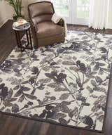 Living room scene with a Waverly Vintage Lux Graphite rug, brown leather chair, and dark wood floors.