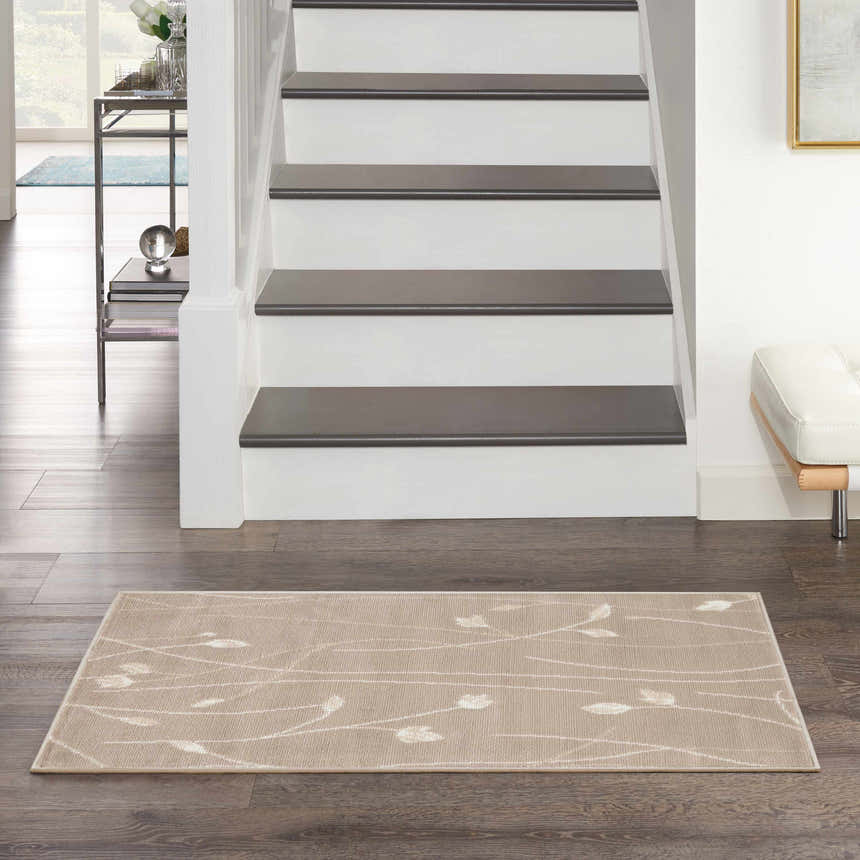 Entryway with stairs and a beige Nourison Grafix area rug with a subtle floral pattern on dark wood floors.