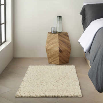 Bedroom scene with a Calvin Klein Riverstone ivory wool rug, wood nightstand, and gray bedding.