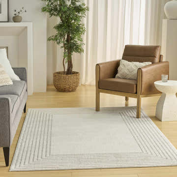 Living room scene with a Nourison Ivory Hues Ivory Grey rug, gray sofa, chestnut chair, and a potted tree. Modern style.
