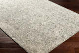 Close up of the hand loomed Abiba Area Rug in beige, black and taupe on dark wood flooring. Corner