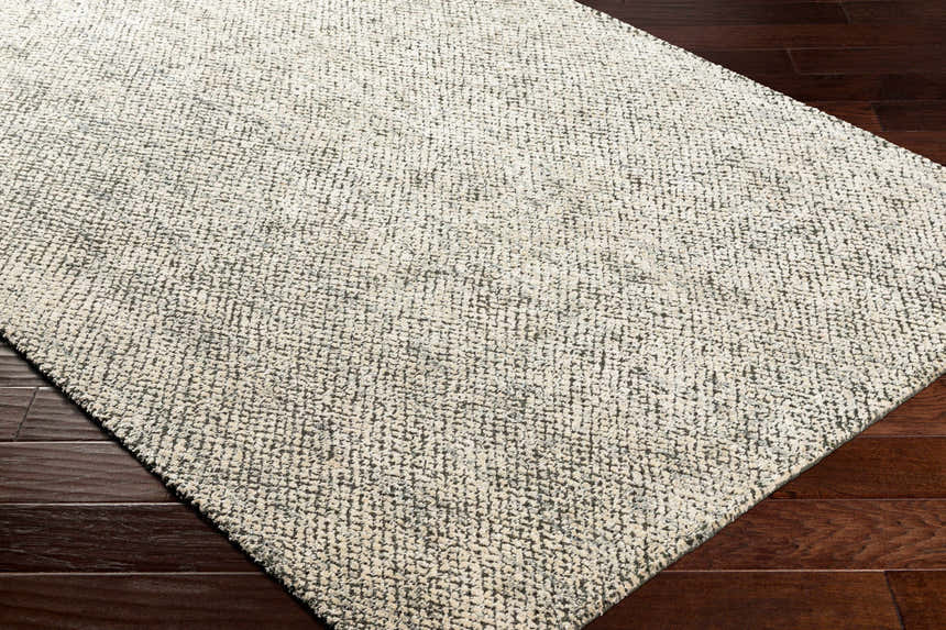 Close up of the hand loomed Abiba Area Rug in beige, black and taupe on dark wood flooring. Corner