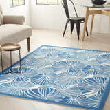 Living room scene with a Waverly Sun N' Shade Blue Tropical Area Rug, beige armchair, wood table, and modern dining set.