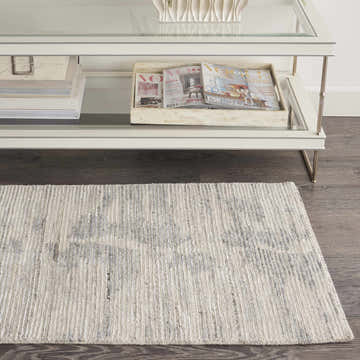 Living room detail with Nourison OCEAN Ivory Slate rug under a glass coffee table on dark wood floors.