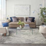 Living room scene with a Nourison Passion Charcoal Ivory rug, taupe sofa, glass table, and white brick wall.