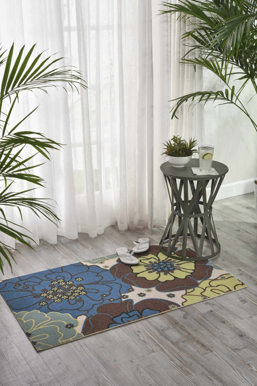 Light blue Nourison Home & Garden rug with floral pattern in a bright, airy room with side table and plants.
