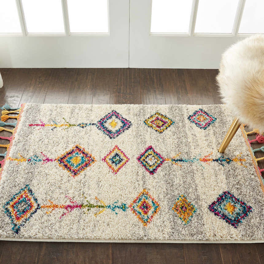 Living room scene with Nourison Nomad Cream Grey Tribal rug, colorful diamond pattern, wood floors, and a furry chair.