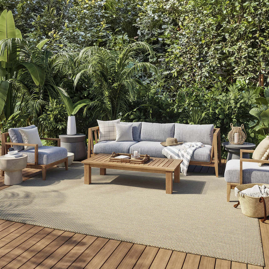 Outdoor patio with gray furniture on a Nourison Courtyard Jute Ivory Modern Area Rug. Lush green plants in the background.