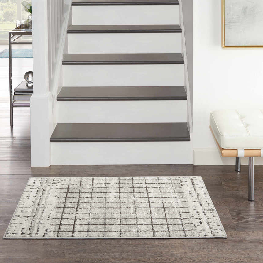 Entryway with Nourison Quarry Ivory Grey rug, dark wood floors, white stairs, and modern white bench.