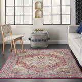 Living room scene with a Nourison Passion Ivory Pink Bohemian rug, light gray sofa, woven chair, and patterned ottoman.