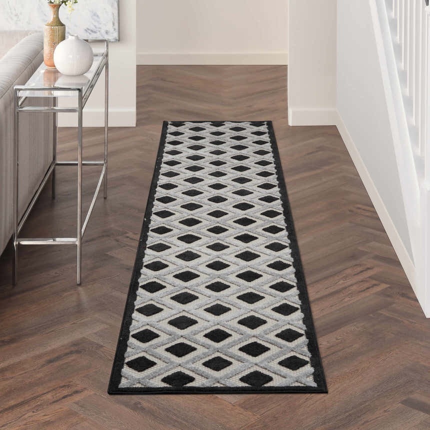 Hallway with Nourison Aloha Black White Modern Area Rug runner on wood floor, console table, neutral walls.