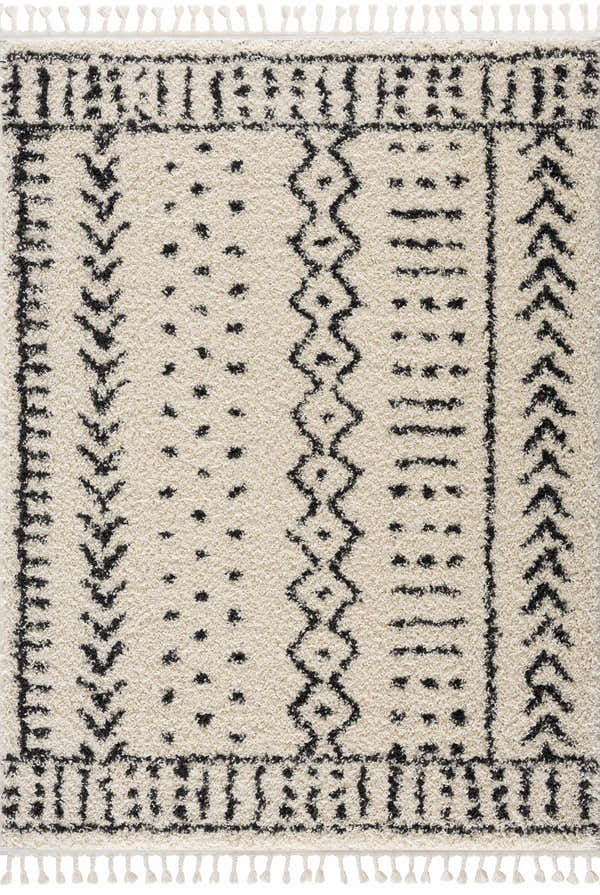 Close-up of the Hauppauge Berber Shag Carpet. Light beige rug with black geometric patterns and tassels. Shag texture. Design-Rectangle-5373