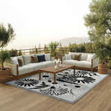 Outdoor patio scene with white sofas, wood table, and Nourison Aloha Black White Outdoor Area Rug.
