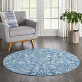 Living room scene with a round Nourison Jubilant Blue Vintage rug, gray chair, wood floors, and a potted plant.