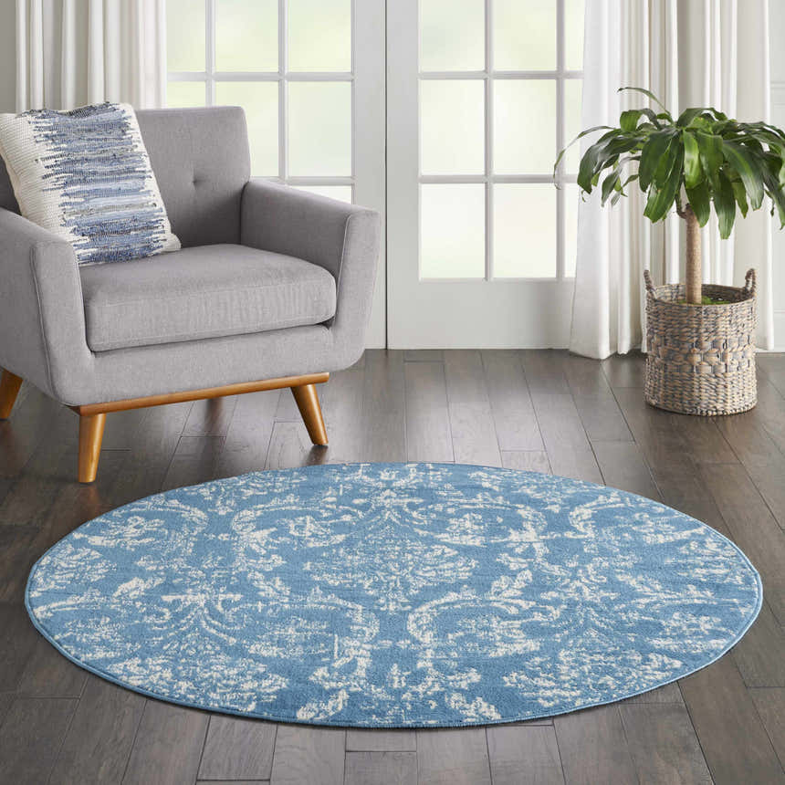 Living room scene with a round Nourison Jubilant Blue Vintage rug, gray chair, wood floors, and a potted plant.