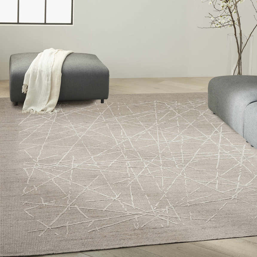 Modern living room with a taupe Calvin Klein CK044 Wander rug, gray ottoman, and light wood floors.