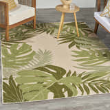 Outdoor patio scene with a Nourison Aloha Ivory Green Area Rug featuring a tropical leaf pattern.