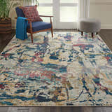 Living room scene with Nourison Fusion Cream Multicolor rug, blue chair, gray ottoman, and plant.