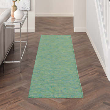 Hallway scene with a Nourison Positano Blue Green rug on dark wood floors, near a glass console table and white walls.