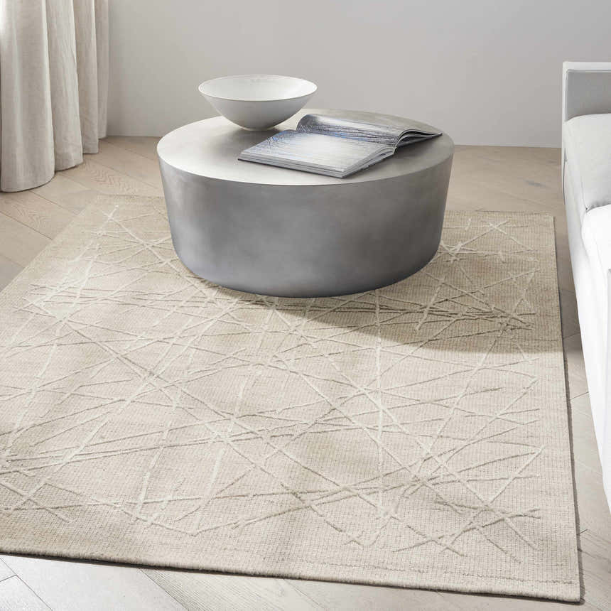 Minimalist living room with taupe Calvin Klein CK044 Wander rug, round coffee table, and neutral sofa.