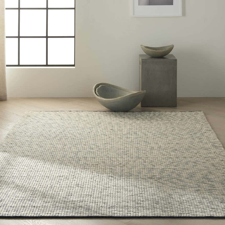 Minimalist room with a Calvin Klein Home Lowland Basalt rug, concrete accents, and natural light.