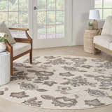 Sunroom with a Nourison Aloha Beige Farmhouse Area Rug, wood furniture, and floral garden view.