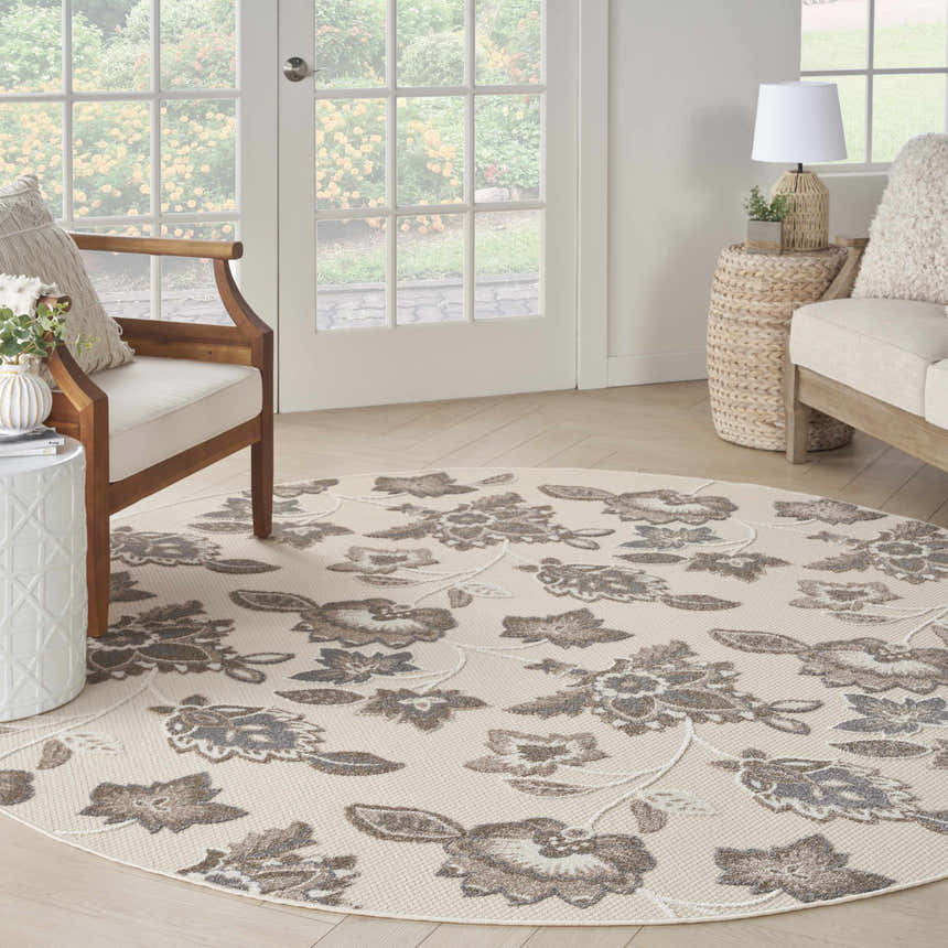 Sunroom with a Nourison Aloha Beige Farmhouse Area Rug, wood furniture, and floral garden view.