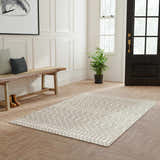 Entryway with Nourison Astra Sage Bohemian Rug, wood bench, herringbone floors, and black door.