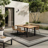 Outdoor patio with wood table, woven chairs, and Nourison Horizon Black Modern Area Rug.