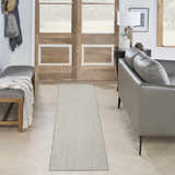 Entryway scene with a Nourison Courtyard Ivory Silver rug, gray leather couch, wood door, and herringbone wood floors.