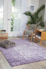 Sunlit room with a Nourison Silk Shadows Amethyst rug, wood floors, chair, and plant for a vintage, relaxed feel.