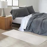 Modern bedroom scene with a Calvin Klein CK024 Irradiant Ivory rug, wood nightstand, and gray bedding.